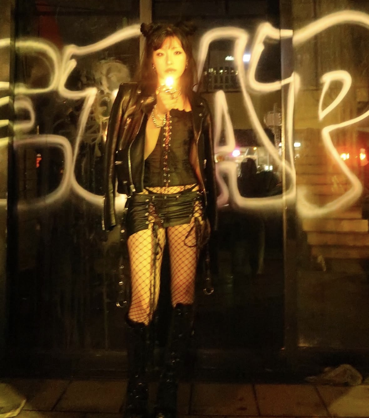 Model in a leather, lace-up, and fishnet look framed by graffiti